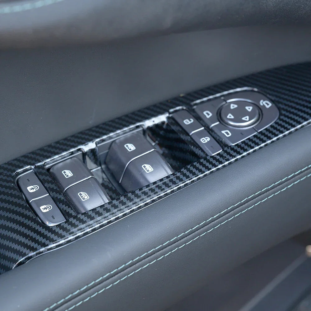 Close-up of a black carbon fiber interior trim for car door window control panel.