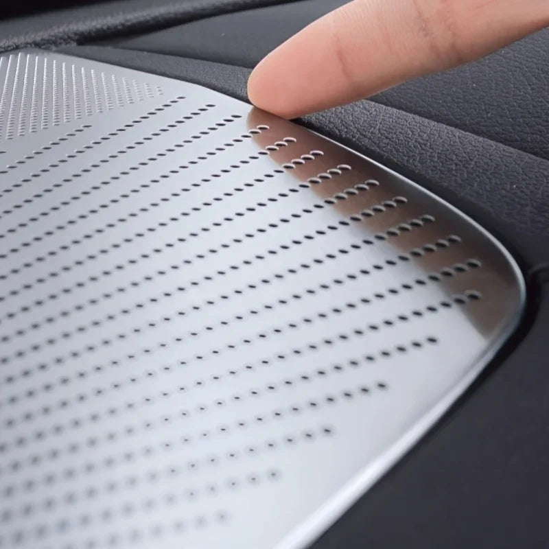 Silver perforated stainless steel trim plate installed on black leather car interior surface.