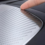 Silver perforated stainless steel trim plate installed on black leather car interior surface.