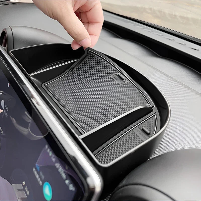 Hand placing a black textured rubber anti-slip mat into a car center console tray.