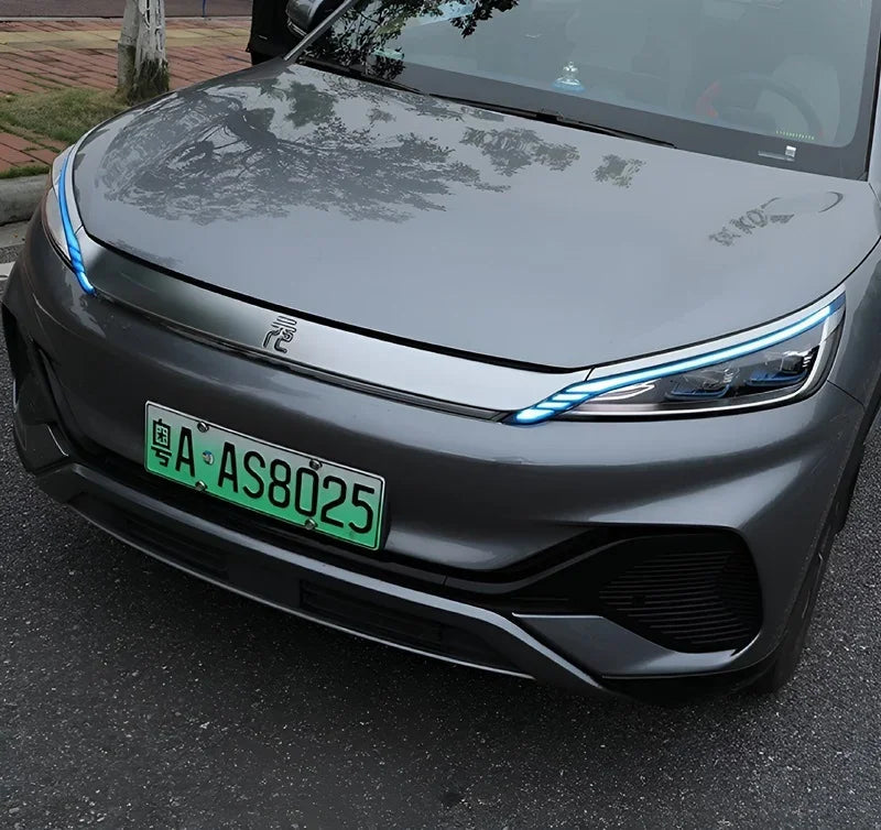 Front view of a sleek grey BYD electric car featuring distinctive blue LED headlights and a green license plate.