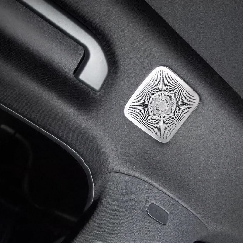 Close-up of a square silver metal perforated speaker grille integrated into a black car interior.