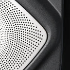 Close-up of a silver perforated metal speaker grille on a textured black automotive component.