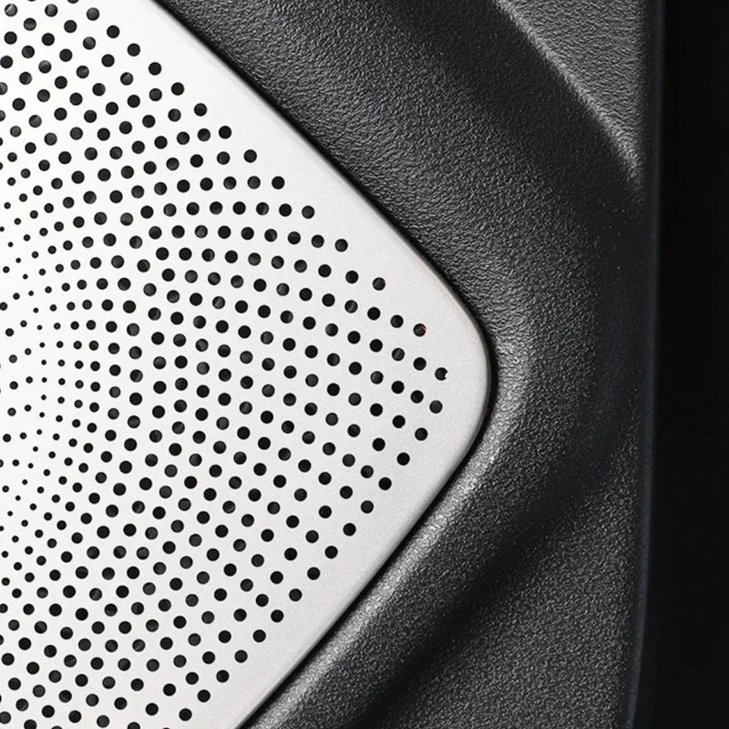 Close-up of a silver perforated metal speaker grille on a textured black automotive component.