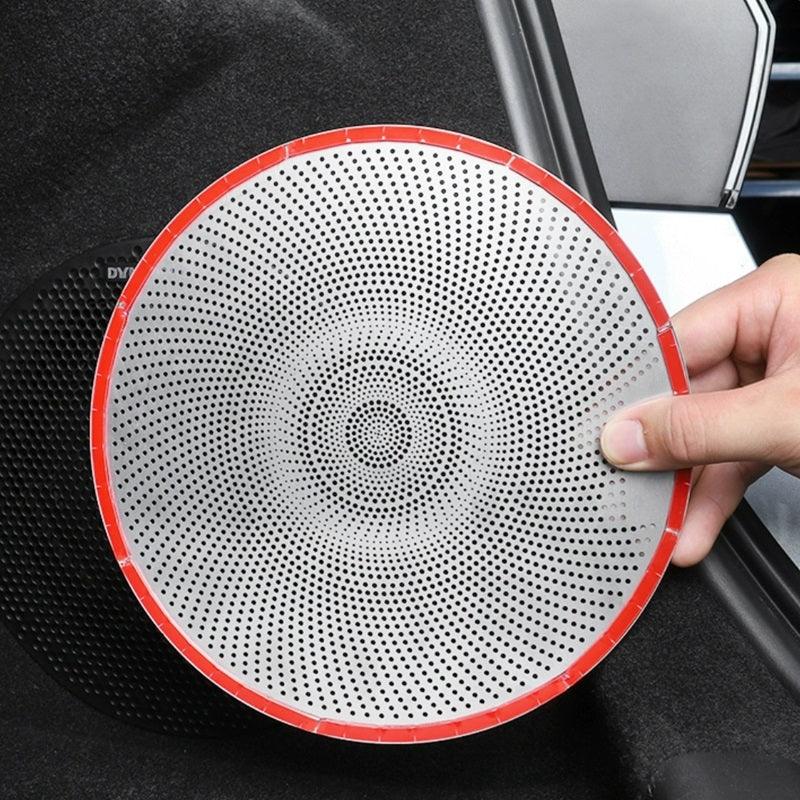 A white circular perforated metal speaker grille with a red rim held by a hand.