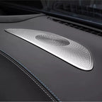 Silver metallic patterned speaker grille installed on a black leather car dashboard.