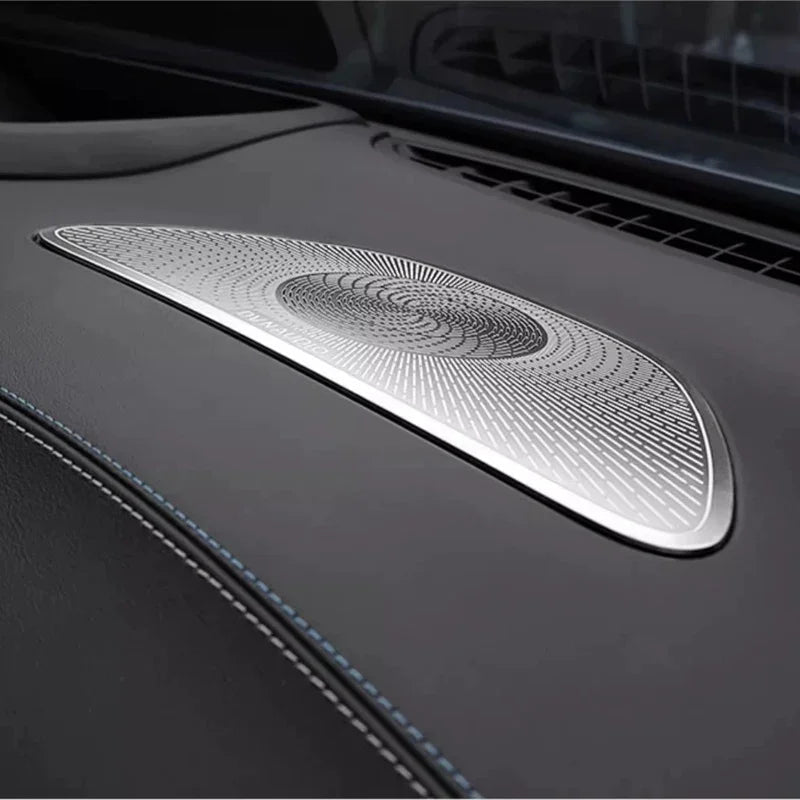 Silver metallic patterned speaker grille installed on a black leather car dashboard.