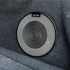 Black circular Dynaudio car speaker grille with a fine metallic mesh pattern.
