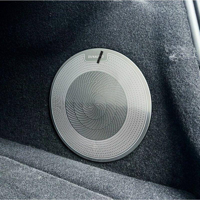 Silver metallic circular speaker grille with a textured concentric pattern on dark grey car interior fabric.