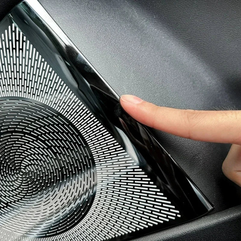 Close-up of a high-gloss black polished speaker grille cover with a patterned metallic texture for car interior protection.