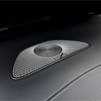 Black textured premium speaker grille with silver concentric ring design on leather interior.