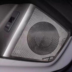 Silver and black metallic Dynaudio car speaker grille with a textured circular pattern.