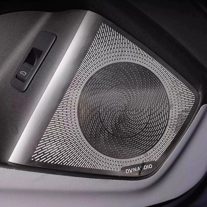 Silver and black metallic Dynaudio car speaker grille with a textured circular pattern.