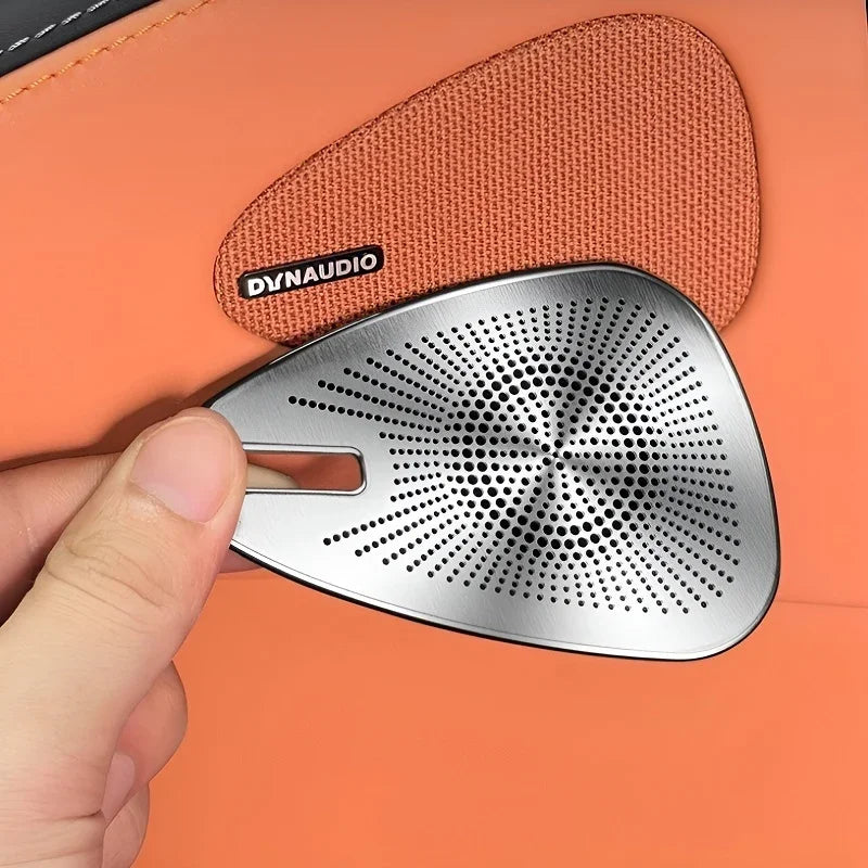 Silver brushed metal Dynaudio speaker grille held against orange fabric interior.