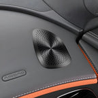 Black textured speaker grille integrated into a grey leather car interior with orange stitching.