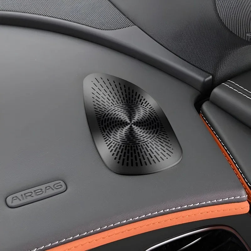 Black textured speaker grille integrated into a grey leather car interior with orange stitching.