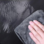 Hand wiping a black textured faux leather car interior surface with a grey microfiber cloth.