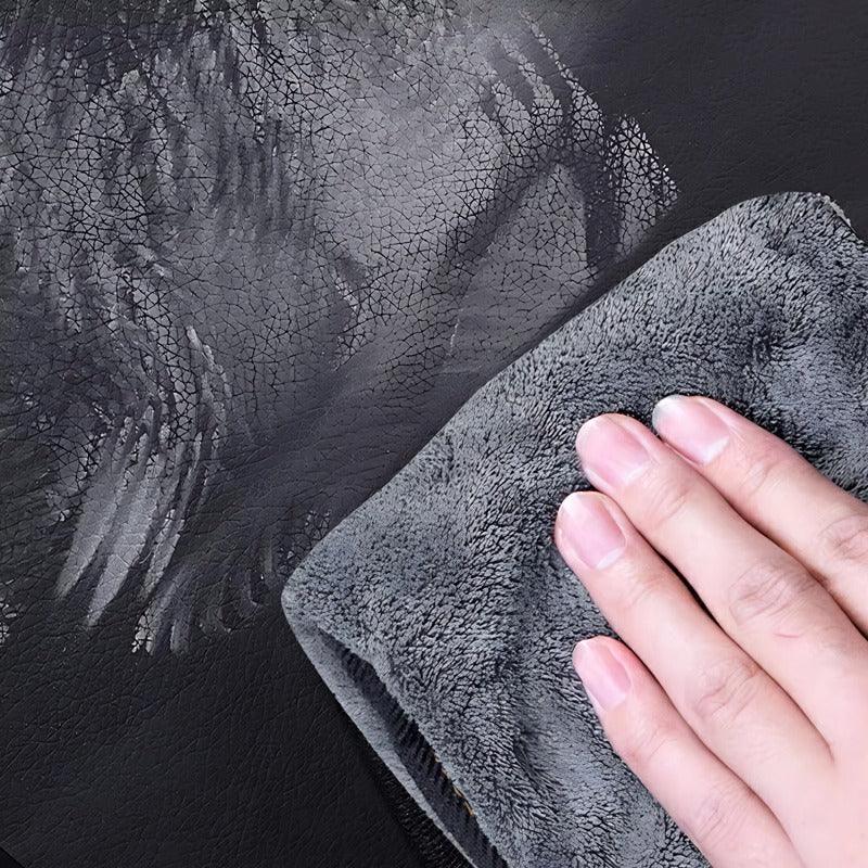 Hand wiping a black textured faux leather car interior surface with a grey microfiber cloth.