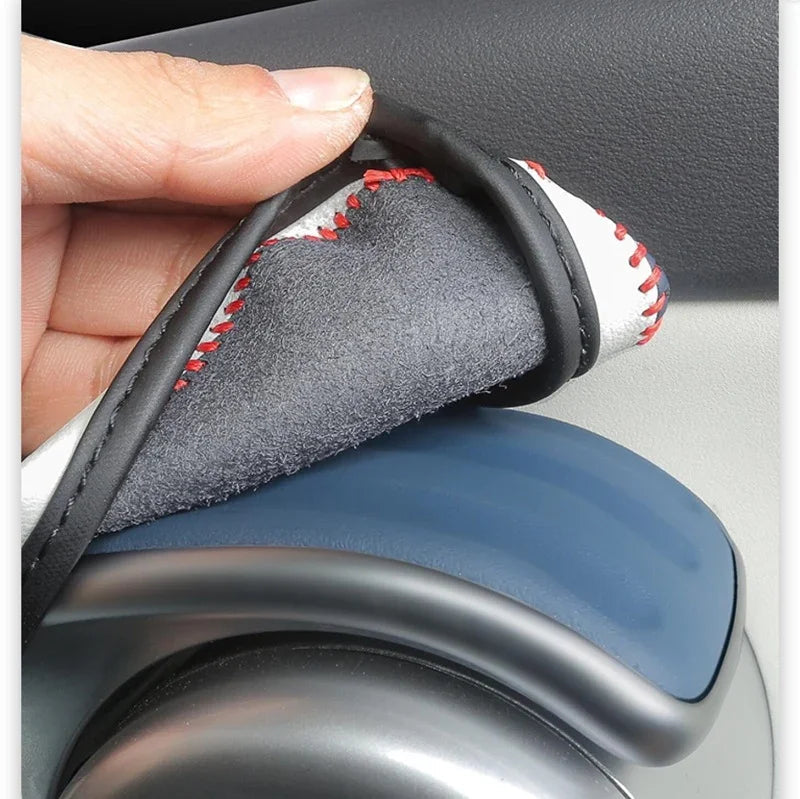 Hand lifting a white and black leather handbrake cover with red stitching for BYD car interior.
