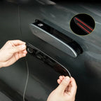 Hands installing a glossy black protective door handle cover on a grey car door.
