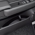 Black leather car door panel with white stitching and integrated storage compartment.