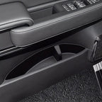 Black leather car door panel with white stitching and integrated storage compartment.