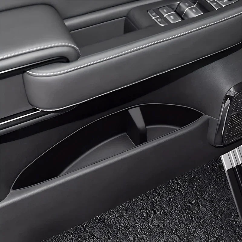 Black leather car door panel with white stitching and integrated storage compartment.