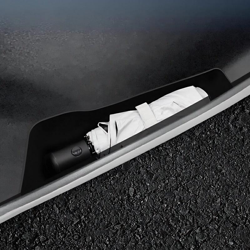 Black car trunk umbrella storage compartment with a white folded umbrella inside