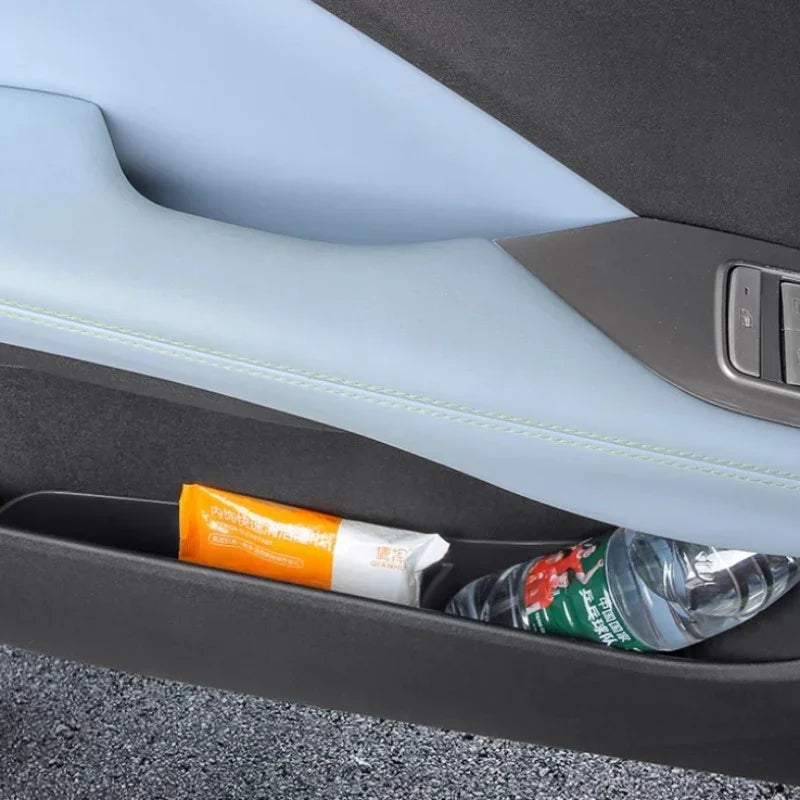 Light blue leather car door panel with a built-in storage compartment holding a snack and water bottle.