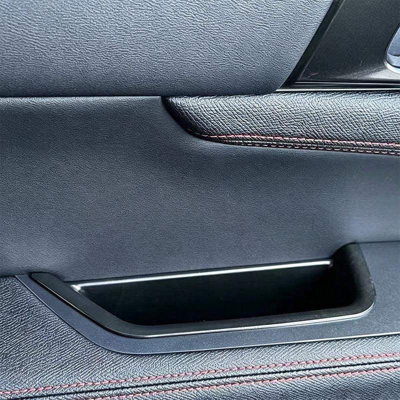 Black leather car door panel with premium texture and red contrast stitching.