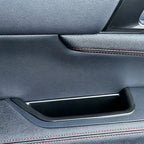 Black leather car door panel with premium texture and red contrast stitching.