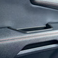 Premium black textured leather car door panel with elegant red contrast stitching.