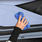 A hand using a blue microfiber cloth to clean the light blue car exterior surface.