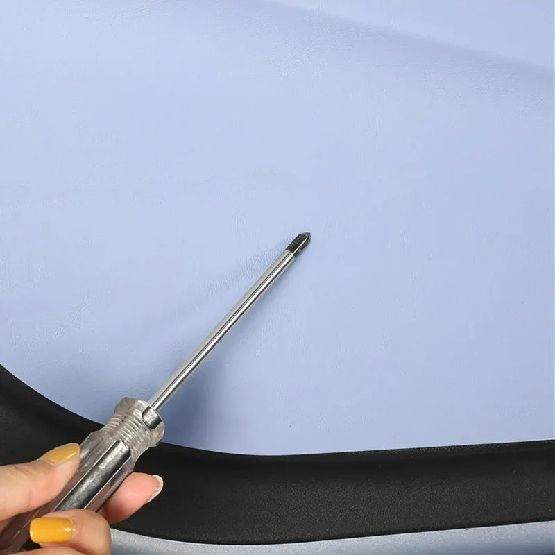 A metal screwdriver being used to install a light grey leather car seat cover.
