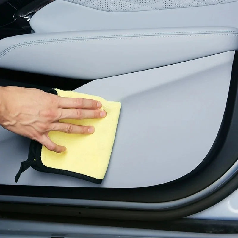 Hand cleaning a light grey car door panel with a soft yellow microfiber cloth.