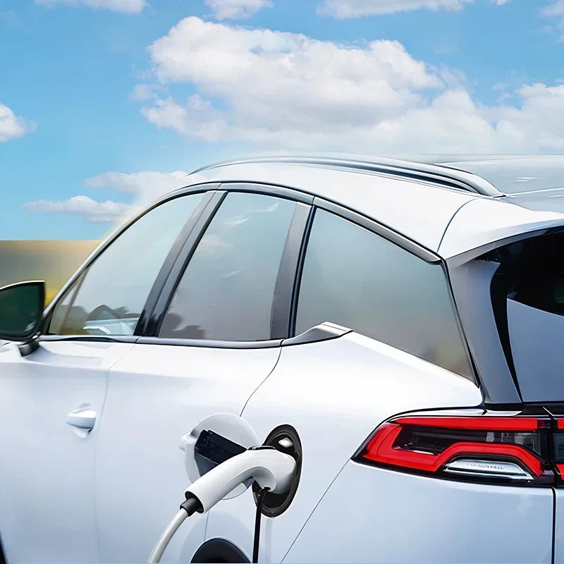 Side view of a white electric vehicle charging outdoors under a bright blue sky.
