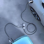 Top view of an electric car being charged via a black power cable connected to a white wall outlet on a grey concrete ground.