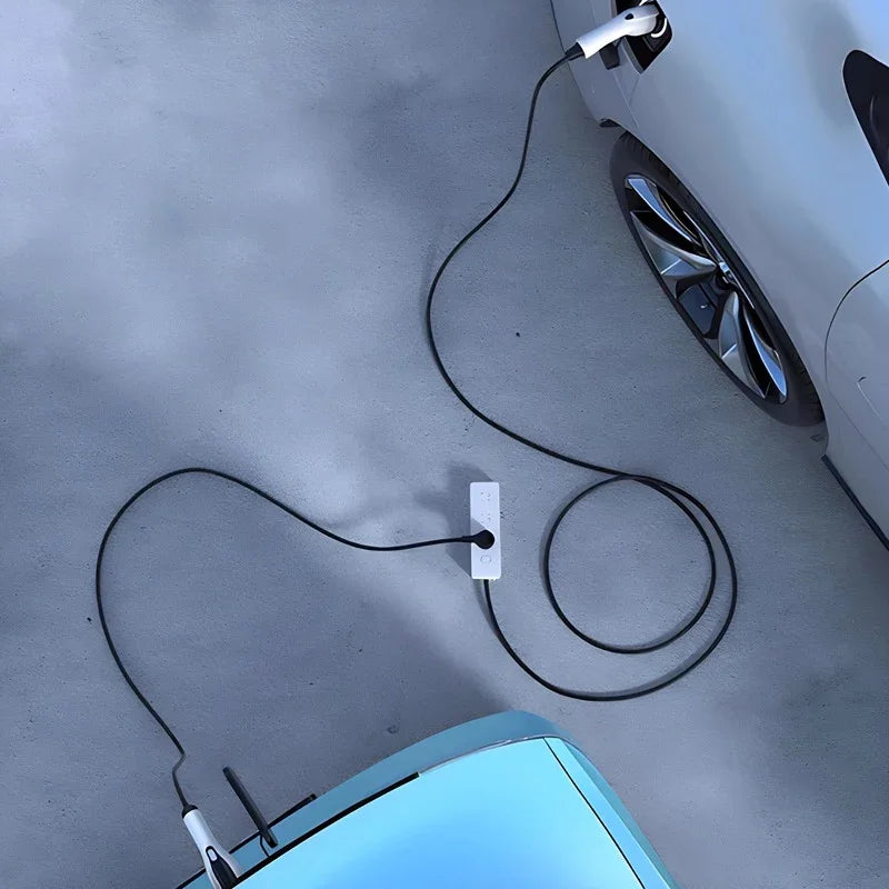 Top view of an electric car being charged via a black power cable connected to a white wall outlet on a grey concrete ground.