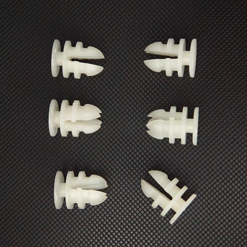 Six white plastic expansion wall plugs for automotive accessories on a textured black surface