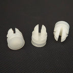 Three white plastic automotive trim clips with a slotted design on a dark textured background.