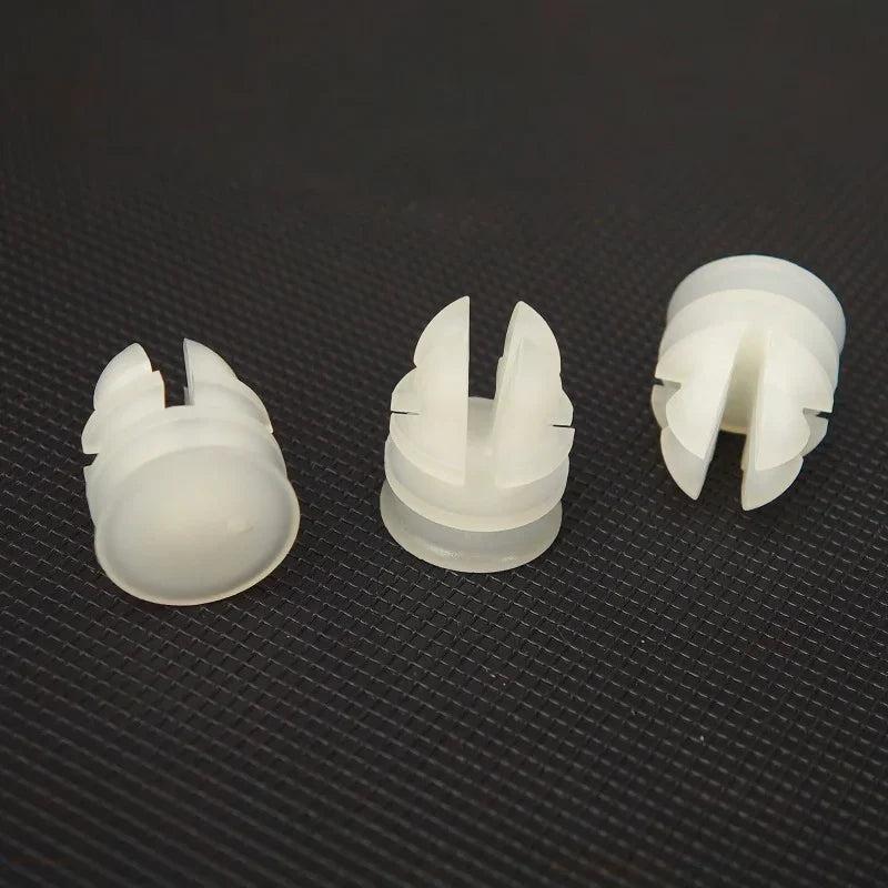 Three white plastic automotive trim clips with a slotted design on a dark textured background.