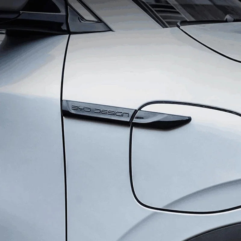 Black matte BYD design emblem on a silver car charging port cover.