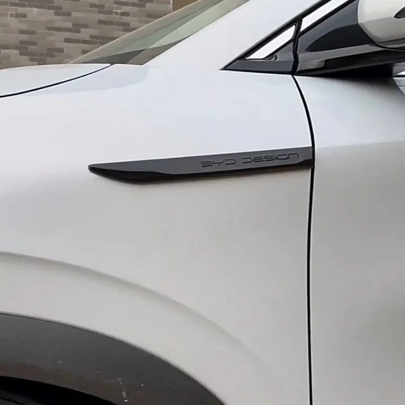 Close-up of a black BYD DESIGN emblem mounted on a white car body.