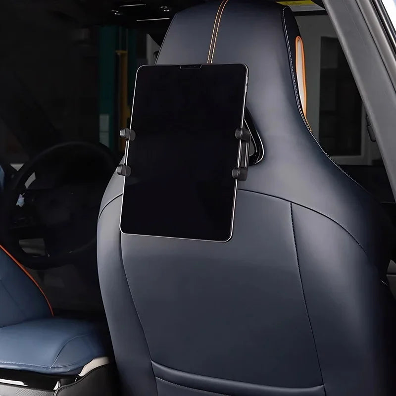 Black tablet mounted on a navy blue leather car seat headrest with orange stitching.