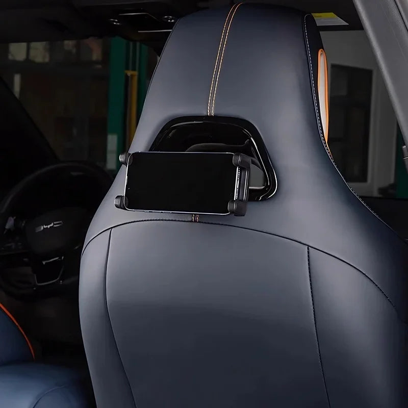 Black smartphone mounted on a headrest holder attached to a navy blue leather car seat with orange stitching.