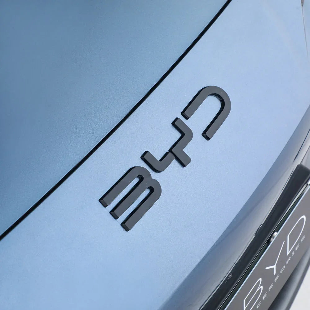 Close-up of a black BYD emblem mounted on a matte blue car body surface.