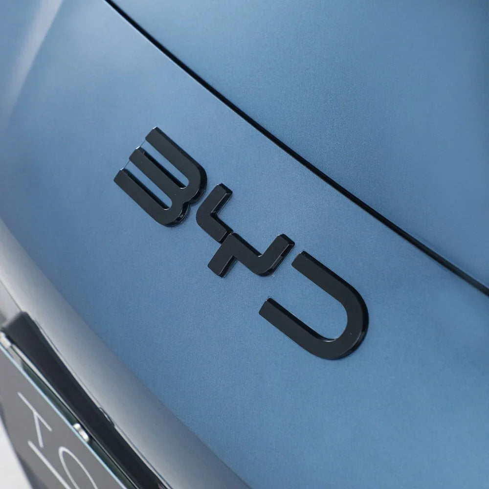 Close-up of the sleek black BYD emblem mounted on a matte blue car body.