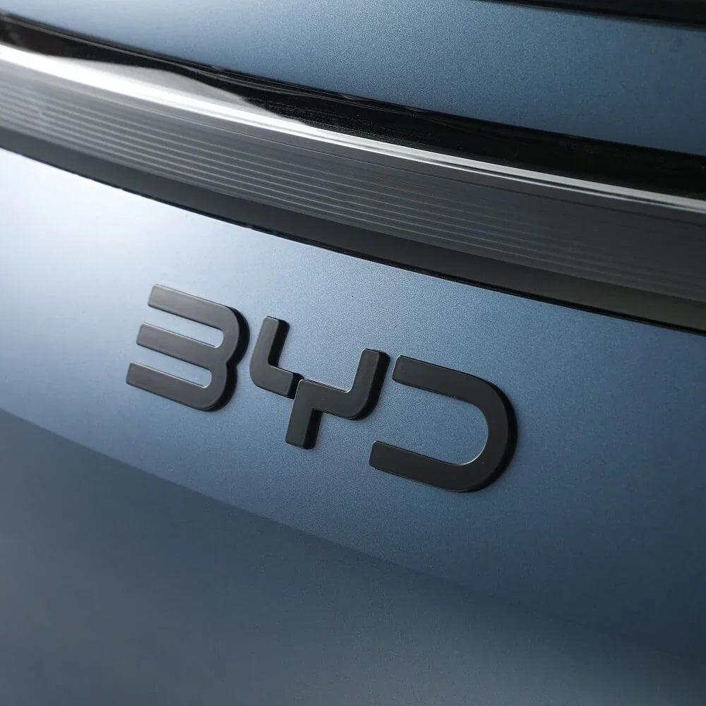 Close-up of a matte black BYD emblem on a metallic blue car body.