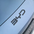 Matte black BYD emblem mounted on a sleek light blue metallic car body.