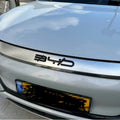 Close-up of a silver BYD car hood featuring a bold, black 3D logo emblem.